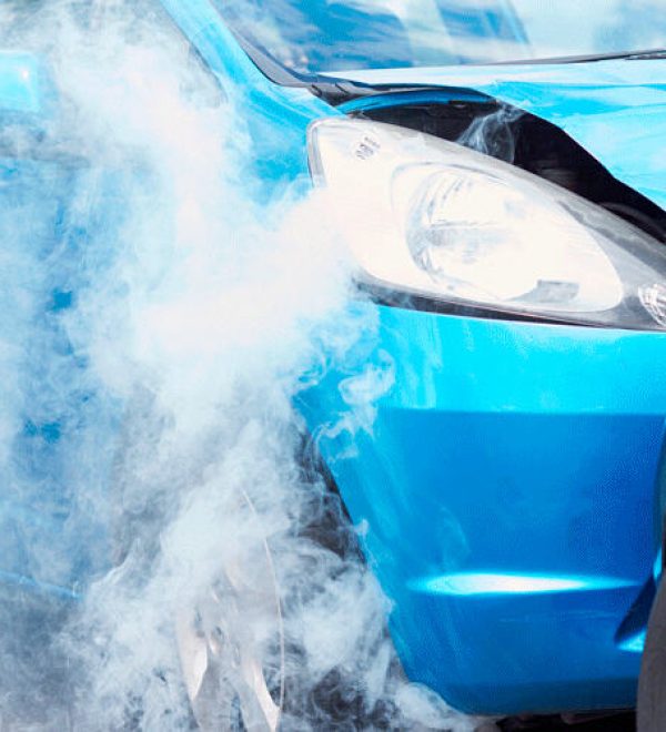 Blue car with smoke rising from a head-on collision with a black car after a traffic accident.