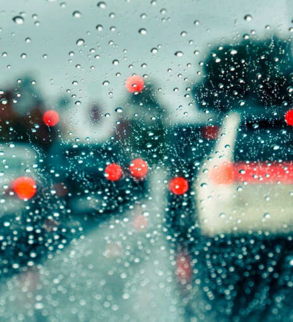 Rain-covered windshield showing blurred traffic and red brake lights during inclement weather in Texas.
